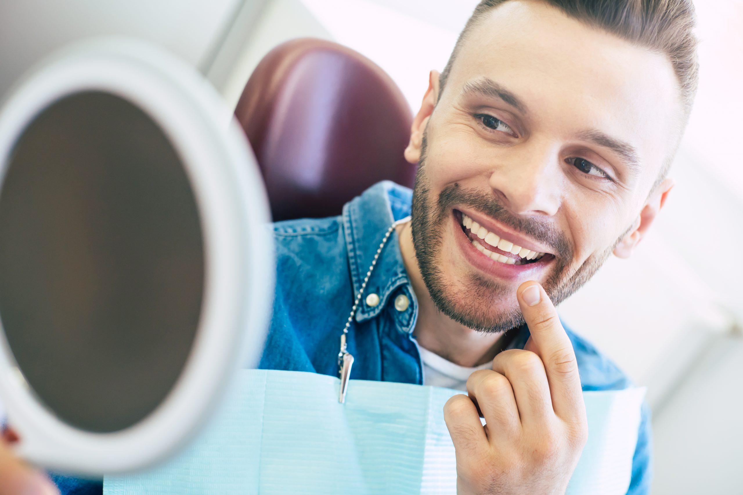 A mirror in a hand of a nice-looking man with a perfect smile which he is using for checking the final look of his smile.