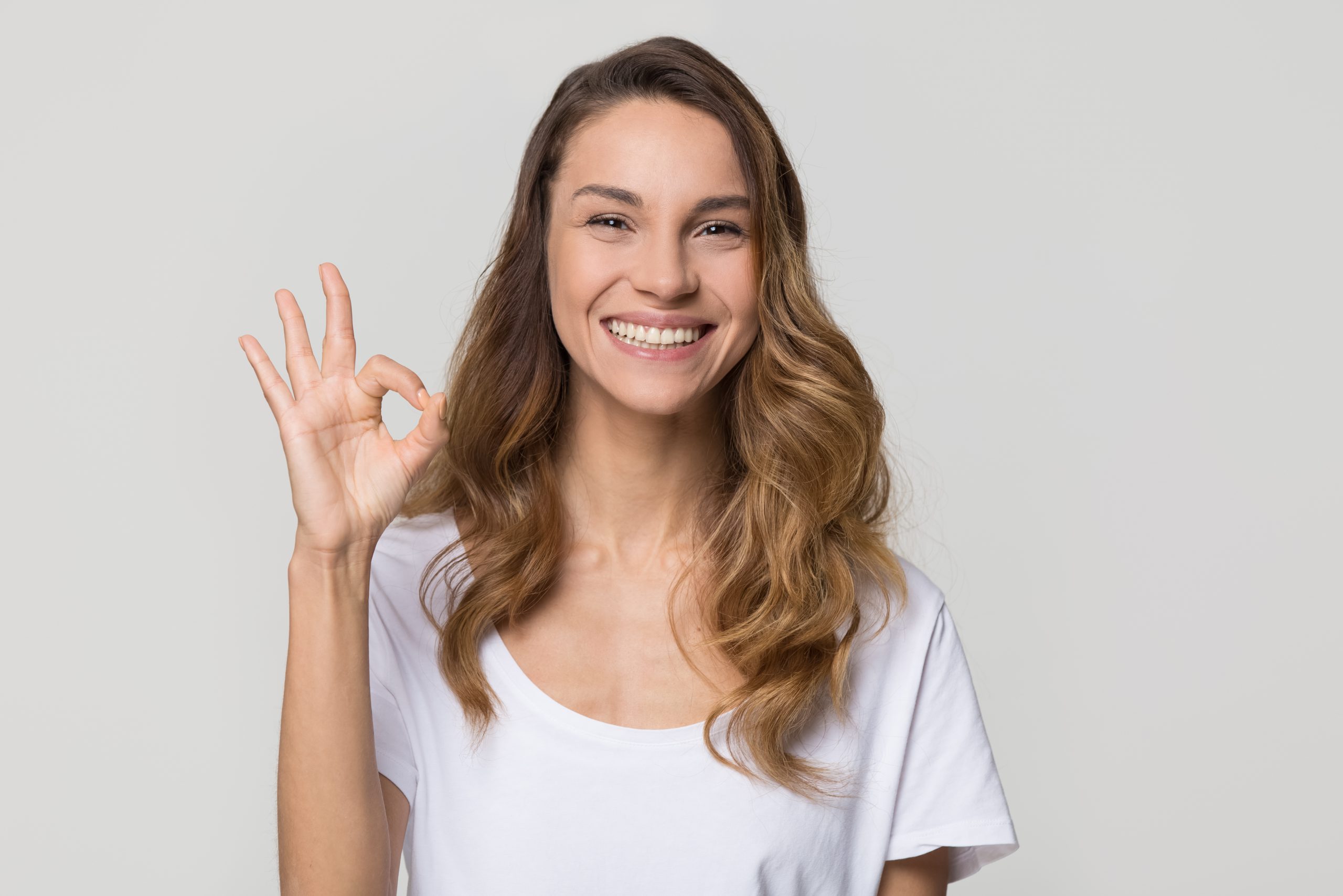 Happy woman gesturing ok smiling with white teeth looking at camera isolated on studio blank background, pretty girl hand showing okay sign satisfied with dental orthodontic service concept, portrait